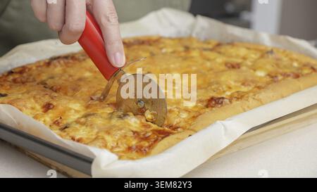 Tagliare la pizza con un coltello rotondo. Primo piano della deliziosa pizza tagliata a pezzi. Affettare al rallentatore una pizza in più fette con una cu Foto Stock