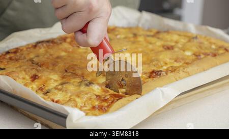 Tagliare la pizza con un coltello rotondo. Primo piano della deliziosa pizza tagliata a pezzi. Affettare al rallentatore una pizza in più fette con una cu Foto Stock