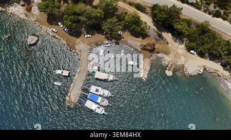 Immagine aerea dall'alto verso il basso che mostra le barche ancorate lungo una costa rocciosa con acqua turchese, circondate da vegetazione lussureggiante e terreno naturale Foto Stock