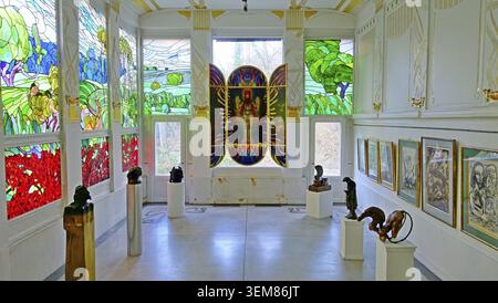 La sala Adolf Boehm espone vivaci vetrate colorate raffiguranti scene e figure pastorali, con un pannello religioso centrale. Busti e sculture sono d Foto Stock