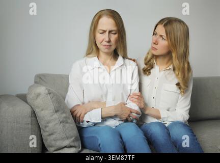 Sconvolta ha offeso due donne caucasiche, madre o sorella matura e figlia adulta che piangono insieme sedute sul divano a casa Foto Stock
