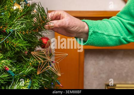 Donna che decora un albero di Natale appesa un ornamento a stella d'oro su un ramo circondato da luci festose Foto Stock