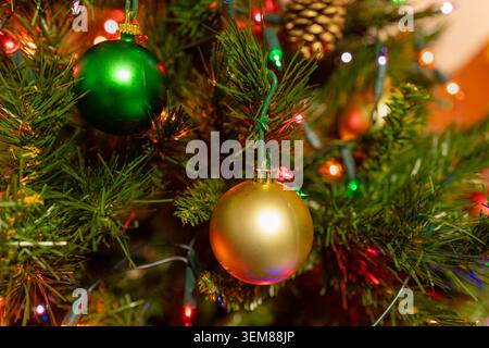Baule dorate e verdi appese ad un albero di Natale decorato circondate da colorate luci festive e rami sempreverdi Foto Stock