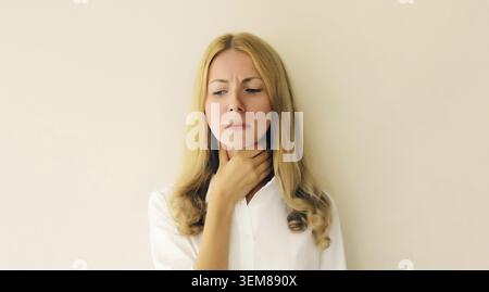 Ritratto di una giovane donna stanca e malata che soffre di mal di gola acuto, tocca il collo con la mano, si sente male Foto Stock