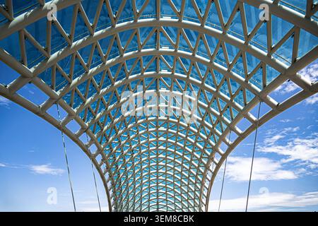 Vista architettonica ad angolo basso di un ponte pedonale contemporaneo caratterizzato da un'elegante struttura a reticolo in acciaio, pannelli di vetro e una sorprendente simmetria. IDE Foto Stock