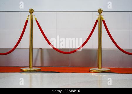I montanti in metallo oro e una corda di velluto formano un sentiero sul tappeto rosso vicino alla parete piastrellata per organizzare le code all'ingresso del cinema. Foto Stock