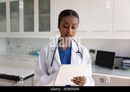 Serio afroamericano medico donna che sfoglia le cartelle cliniche su tablet Foto Stock