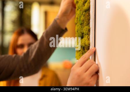 Primo piano di una coppia che mette decorazioni sul muro nella loro nuova casa, creando un'atmosfera accogliente personale all'interno della prima casa. Proprietari di case che godono della soddisfazione di ridecorare e sistemarsi. Foto Stock