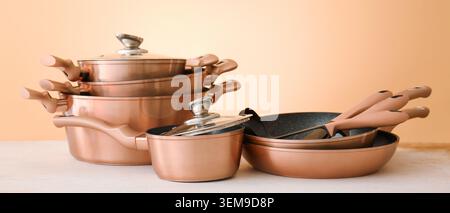 Set di utensili da cucina in oro rosa con padelle, pentole e coperchi in vetro disposti sul bancone della cucina su un caldo sfondo beige Foto Stock