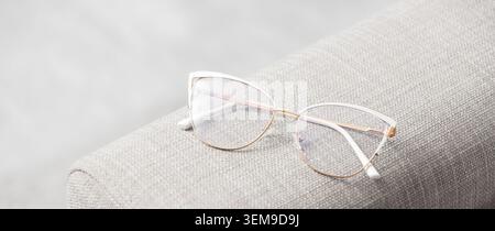 Eleganti occhiali da vista Cat-eye sul bracciolo del divano in tessuto leggero, con luce naturale soffusa, gli occhiali interni minimalisti sono ancora più resistenti grazie allo spazio per le copie Foto Stock