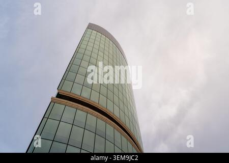Grattacielo che si piega verso l'alto e presenta una moderna facciata in vetro contro un cielo neutro Foto Stock