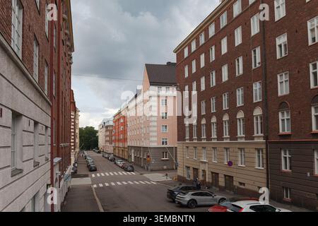 HELSINKI, FINLANDIA - 11 AGOSTO 2025: Lunga strada dritta fiancheggiata da alti edifici residenziali in mattoni con auto parcheggiate in una giornata estiva. Foto Stock