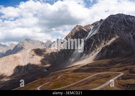 Vista panoramica di una tortuosa strada di ghiaia che conduce attraverso le spettacolari montagne ad alta quota nella Gola di Kegeti, Kirghizistan. Foto Stock