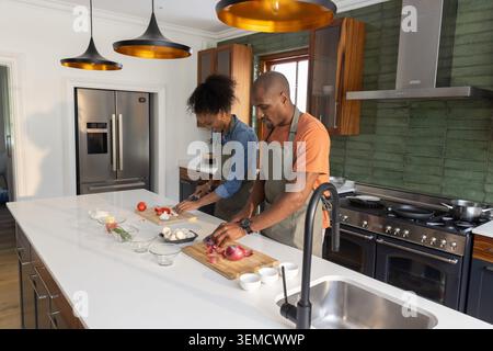 Abbina i pomodori ciliegini e le cipolle sui taglieri di Kitchen Island indossando grembiuli Foto Stock