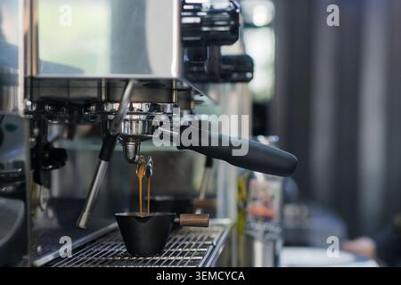Caffè espresso fresco che viene versato dal portafiltro di una macchina da caffè professionale in una piccola caraffa nera in un caffè Foto Stock