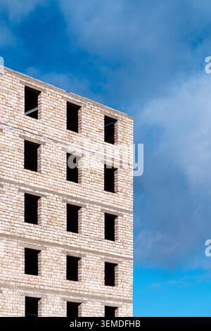 Unfinished multi-storey brick building with empty window openings, captured from below against a blue sky, highlighting raw architecture and urban dev Foto Stock