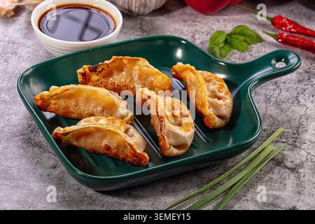 Gnocchi fritti dorati serviti su un piatto di ceramica verde con salsa di soia, peperoncini rossi e cipolle verdi su fondo in pietra. Cucina asiatica Foto Stock