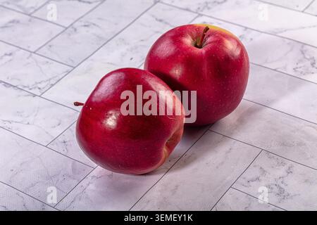 Due mele rosse mature poste su piastrelle in marmo bianco. Frutta fresca in primo piano con illuminazione naturale e colori vivaci. Concetto di snack salutari Foto Stock