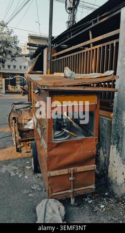 Un vecchio carrello alimentare mobile, con una struttura in legno resistente agli agenti atmosferici e componenti in metallo arrugginito, è parcheggiato su un marciapiede. Foto Stock