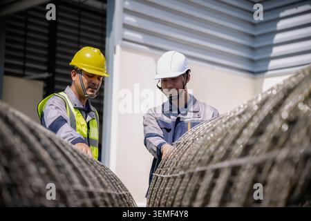 Lavoratori edili asiatici che ispezionano il sito di costruzione della rete metallica d'acciaio, due lavoratori ispezionano i fili avvolti in una struttura industriale. Sono in un'invenzione Foto Stock