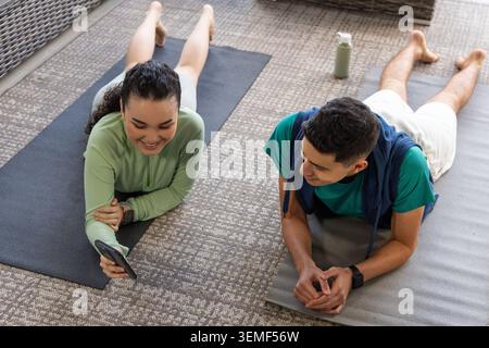 Coppia sdraiata su tappetini da ginnastica in soggiorno, tenendo in mano lo smartphone e indossando abbigliamento sportivo Foto Stock