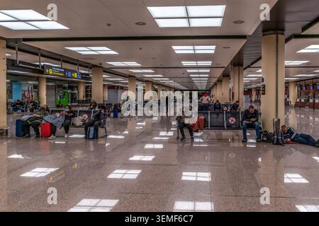 Barcellona, Spagna - 24 novembre 2021: Lounge all'interno dell'aeroporto Josep Tarradellas Barcelona-El Prat. Le persone con bagagli siedono su sedili in metallo Foto Stock
