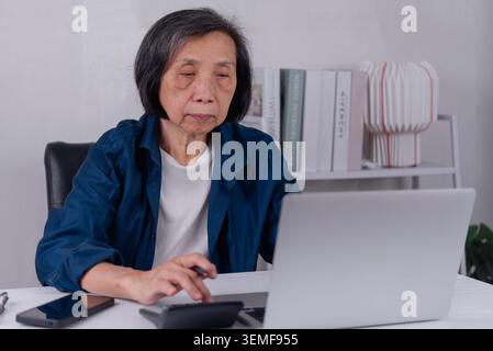 Grave donna asiatica anziana che usa la calcolatrice e il portatile con espressione preoccupata. Pianificazione finanziaria degli anziani, stress derivante dall'inflazione, costi elevati Foto Stock