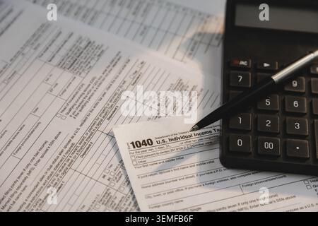 Calcolatrice e penna collocate su moduli fiscali individuali e documenti finanziari per il calcolo di imposte, revisione contabile, preparazione dei pagamenti e spese Foto Stock