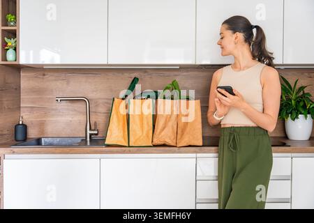 Donna che utilizza l'app per smartphone per gestire l'ordine di consegna della spesa a casa. Food shopping online e lifestyle digitale Foto Stock