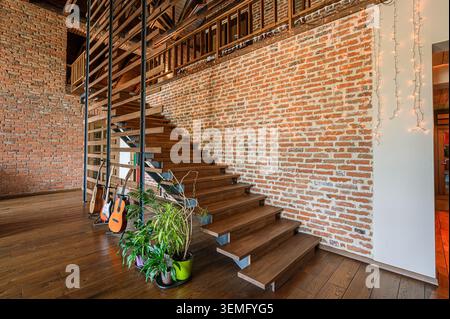 interni moderni in loft con scale in legno, pareti in mattoni, pavimenti in legno duro e chitarre. Le piante aggiungono un tocco di natura. Foto Stock