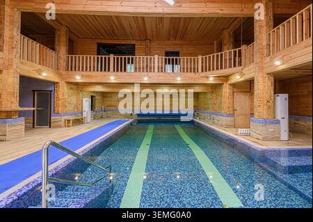 Area piscina coperta con pareti rivestite in legno, piscina con piastrelle a mosaico, balcone e luce naturale. Foto Stock