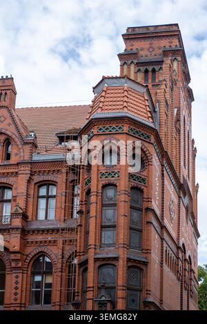 L'edificio storico in mattoni rossi neogotici si erge alto, con finestre ad arco e mattoni decorativi in vetro verde Foto Stock