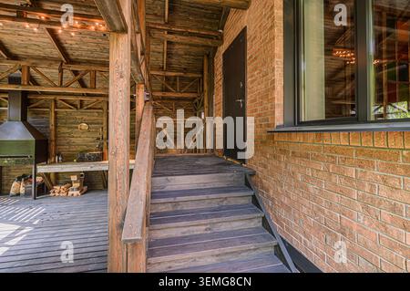 Ponte in legno con scale che conducono ad una casa in mattoni. Griglia e luci visibili sullo sfondo. Foto Stock