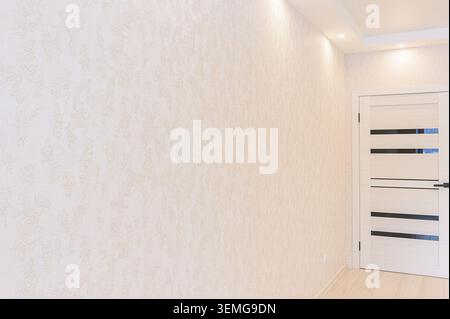 camera vuota e con luce soffusa, caratterizzata da carta da parati a motivi geometrici, una porta moderna con accenti orizzontali e pavimento in legno chiaro Foto Stock