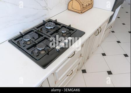 foto ravvicinata di una cucina moderna con una stufa a gas nera installata su un ripiano bianco. Gli armadi della cucina sono visibili sotto. Foto Stock