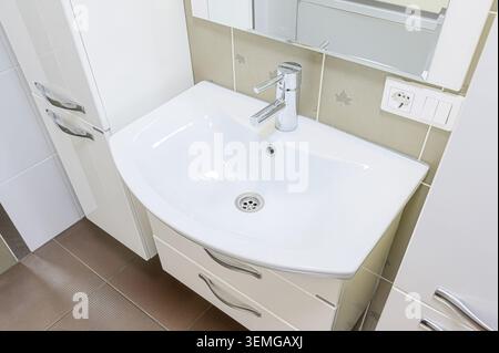 il luminoso lavandino del bagno è dotato di lavello bianco curvo, rubinetto cromato e parete a specchio. Design pulito e moderno. Foto Stock