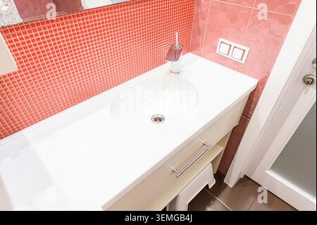 bagno ben illuminato con lavandino bianco, piastrelle a mosaico rosso e piastrelle in tessuto rosa. Foto Stock
