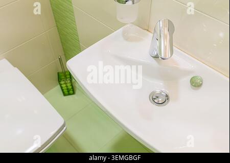 immagine ad angolo alto di un bagno: lavandino con rubinetto cromato, wc e morbide piastrelle verdi. Stile pulito e minimalista Foto Stock