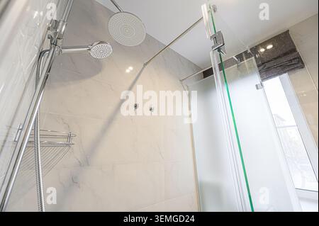 bagno luminoso con doccia con doppio soffione doccia, piastrelle in marmo e porta in vetro smerigliato. Estetica moderna e pulita. Foto Stock
