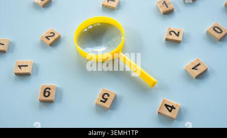 Vista ad angolo alto di una lente d'ingrandimento gialla incentrata su piastrelle in legno sparse, concetto di indagine finanziaria, audit e Market re Foto Stock