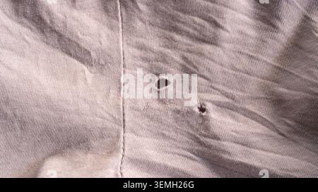 Primo piano di tessuto di cotone grigio usurato con piccoli fori lacerati e bordi sfilacciati vicino alla cucitura Foto Stock