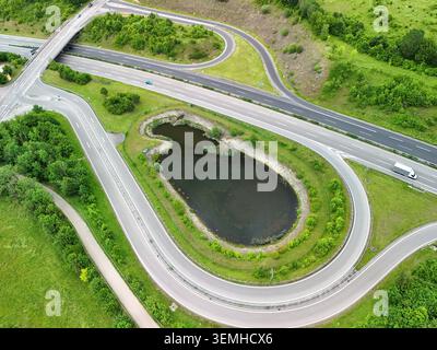 Veduta aerea dello svincolo autostradale con strade curve e laghetto nel paesaggio verde Foto Stock