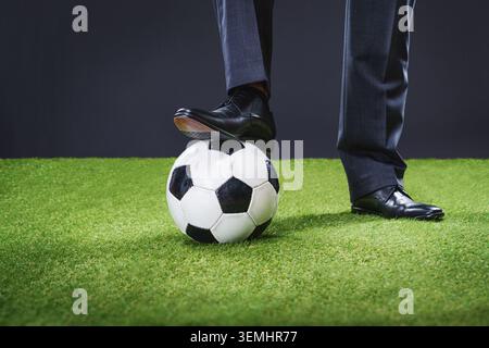 un uomo sportivo in un'elegante tuta con pallone da calcio in un grande stadio - concetto di allenatore o giocatore professionista. Piedi di allenatore di calcio, giocatore calpestare il pallone di calcio Foto Stock
