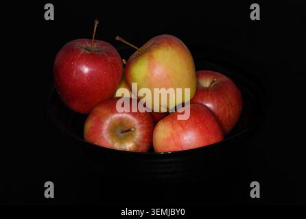 Una ciotola contiene diverse mele rosse e verdi poste su una superficie scura. La frutta è lucida e ordinata, mostrando un mix di colori. Questo semplice displ Foto Stock