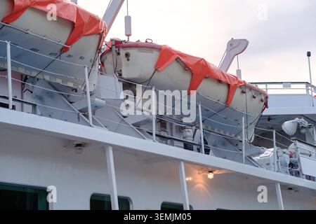 Imbarcazioni di salvataggio fissate sul lato di una nave da crociera con coperture arancioni, che mostrano attrezzature di sicurezza e caratteristiche di design marittimo Foto Stock