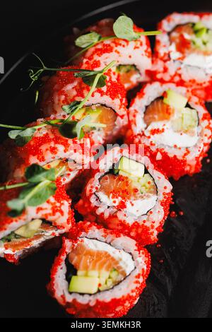 Gli involtini di sushi ripieni di salmone e cetriolo sono disposti su un piatto nero. Sopra i panini c'è un capriolo di pesce rosso brillante. Questo piatto è servito in un restau Foto Stock