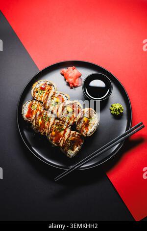 Un piatto presenta diversi sushi roll con condimenti e salse. Wasabi e zenzero sottaceto si siedono accanto al sushi. Due bacchette sono posizionate accanto alla p Foto Stock