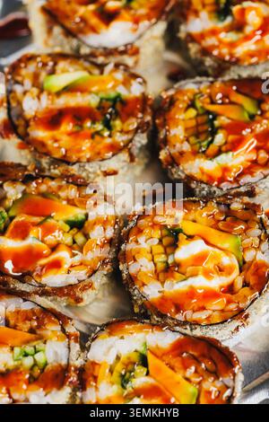 Un piatto contiene diversi panini di sushi ripieni di verdure e frutti di mare. Una salsa piccante viene versata sulla parte superiore, rendendola gustosa. Questo piatto è com Foto Stock