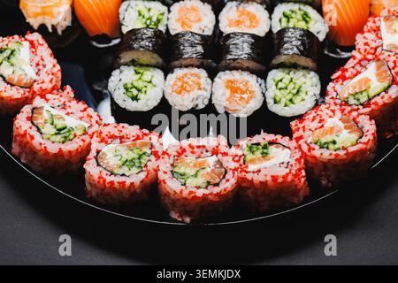 Diversi tipi di sushi roll sono visualizzati su un piatto nero rotondo. Il piatto presenta sushi colorato con vari ripieni e condimenti. Questa scena Foto Stock