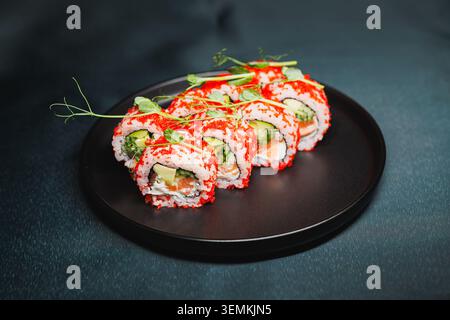 Gli involtini di sushi ripieni di granchio, cetriolo e avocado sono posizionati ordinatamente su un piatto nero. La luce della cucina mette in risalto i colori vivaci dell'ingresso Foto Stock